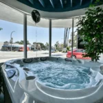 interior photo of the lifestyle outdoor culver city showroom showing a filled hot tub with bubbling water positioned beside the front window, with street views, parked cars, and indoor plants visible around the display.
