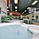 interior photo of the lifestyle outdoor sherman oaks showroom showing a filled hot tub with bubbling water in the foreground, with additional hot tubs, product signs, potted plants, hot spot wall branding, and the pergola-style display area visible behind it.