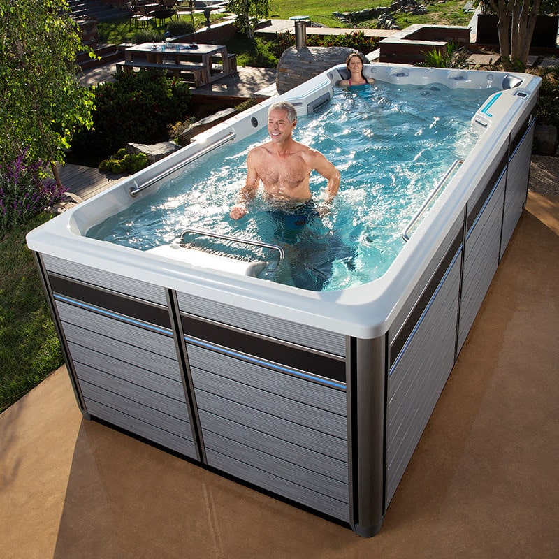 man working out in an endless pool while a young woman relaxes at the other end